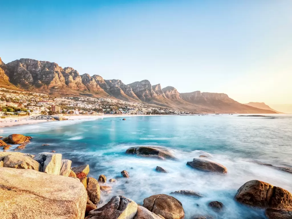 Golden hour at Cape Town's Clifton Beach, framed by the majestic Twelve Apostles mountains and shimmering turquoise waters.