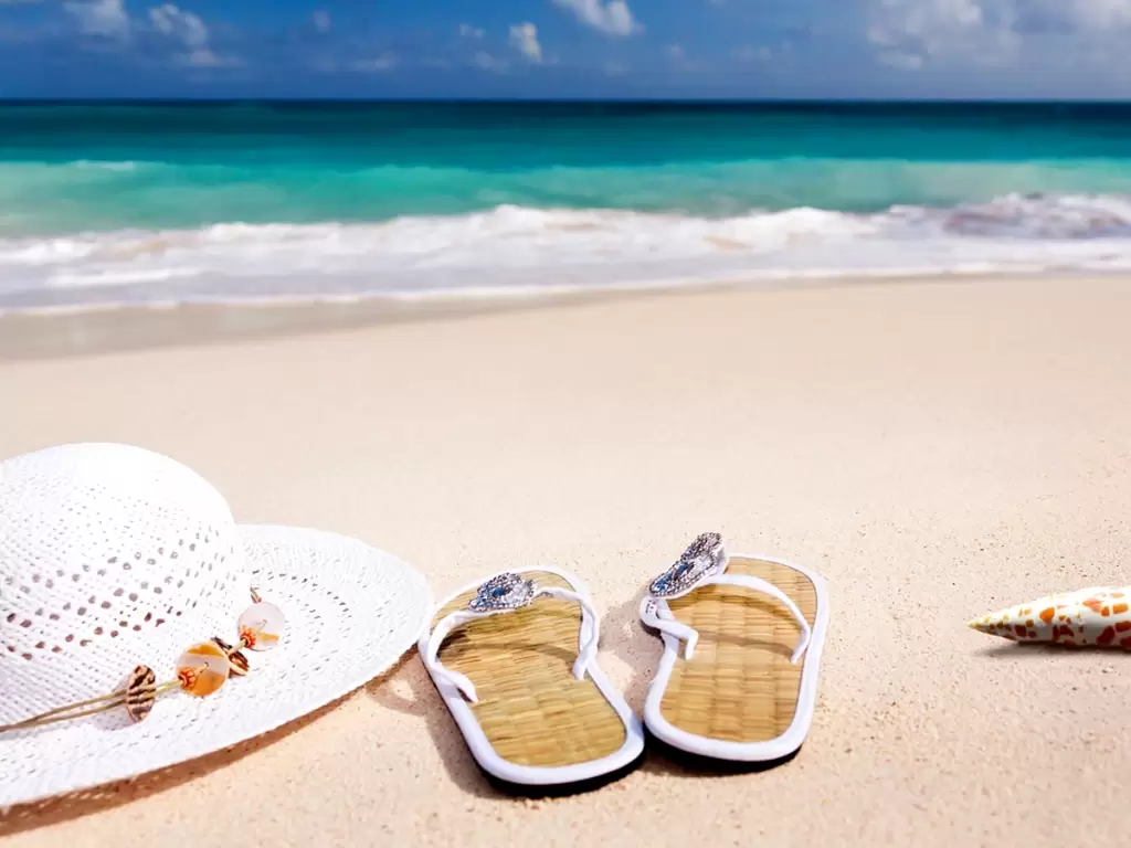 White hat and sandals on a pristine sandy beach of South Africa with turquoise waves gently rolling ashore, evoking a serene tropical getaway.