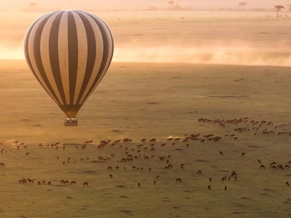Hot air balloon over Serengeti plains during the great migration on a luxury African safari adventure.