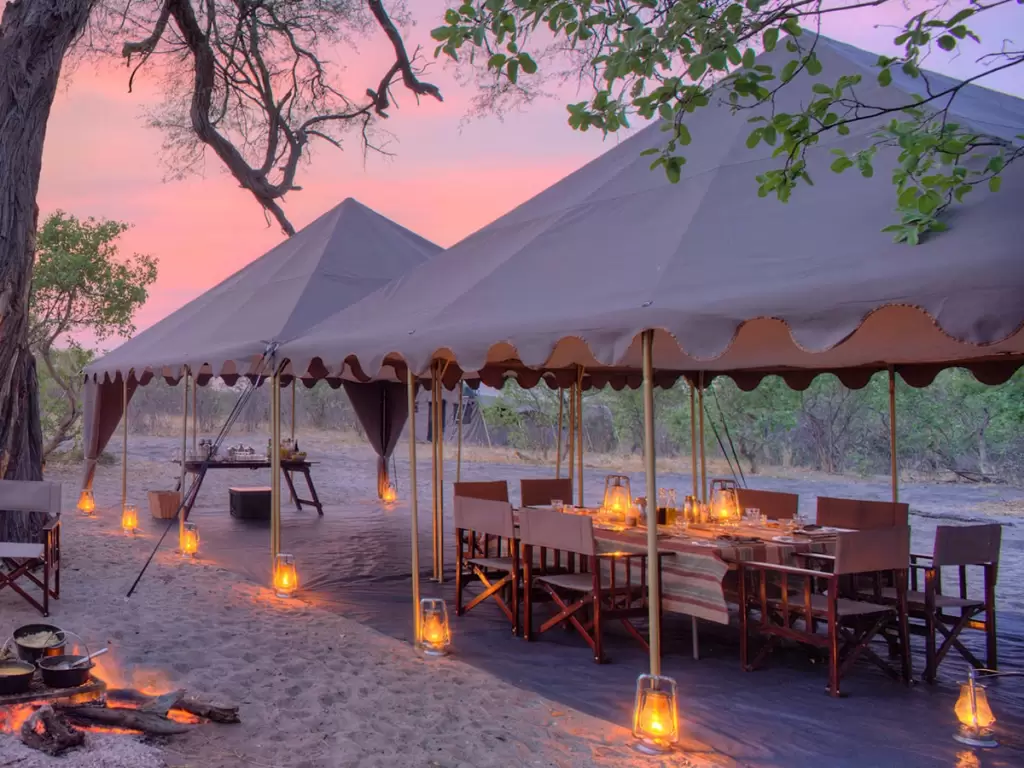 Campfire and lantern-lit dining setup at a mobile tented lodge on a luxury African safari adventure.