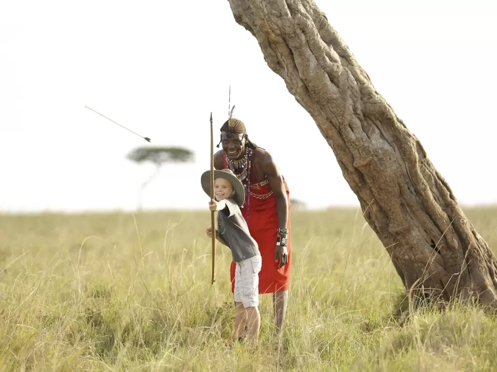 A Maasai warrior teaches a child spear throwing, a cultural activity during kids’ activities on an African safari.