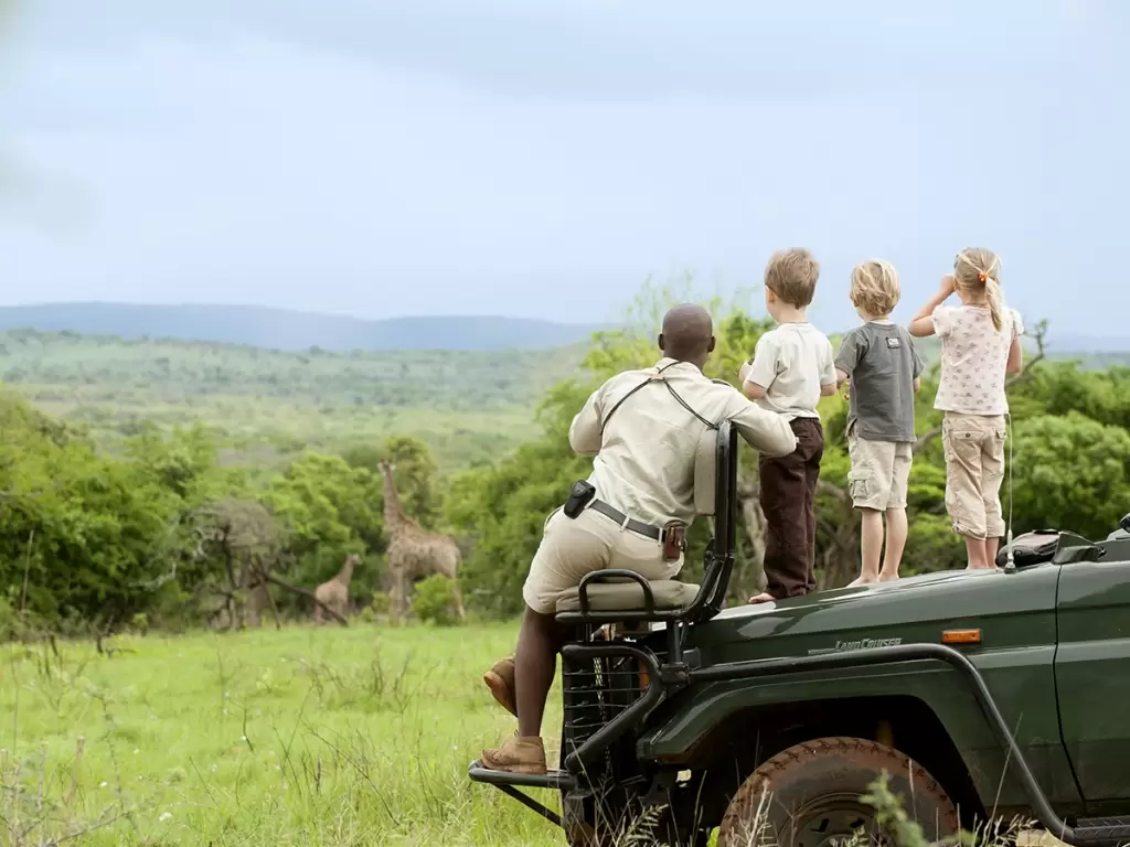 Guide and children spot giraffes during an African safari from a safari vehicle.