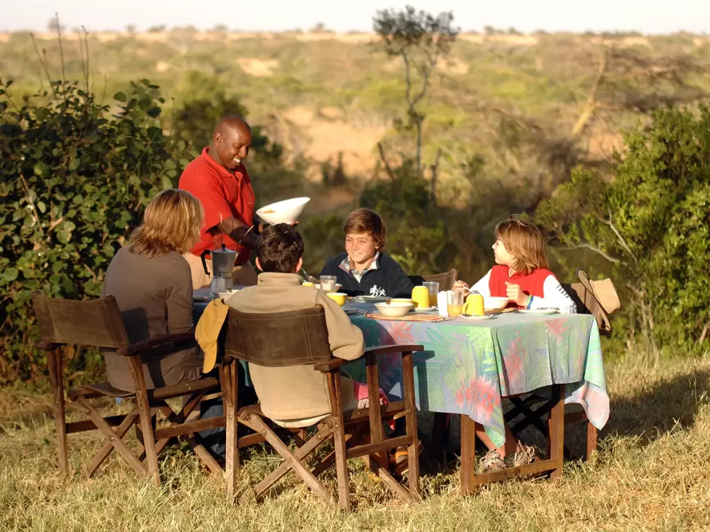 Family enjoys outdoor breakfast on a luxury family safari in Africa, surrounded by pristine wilderness views.