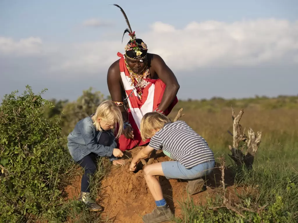 A Maasai guide teaching kids animal tracking, a fun, child-friendly activity on African safari adventures.