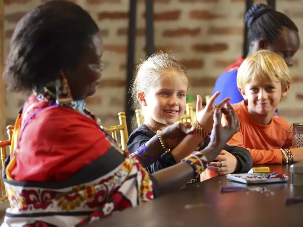 Children learning traditional beadwork from Maasai women on a crafts and beadwork African safari activity.