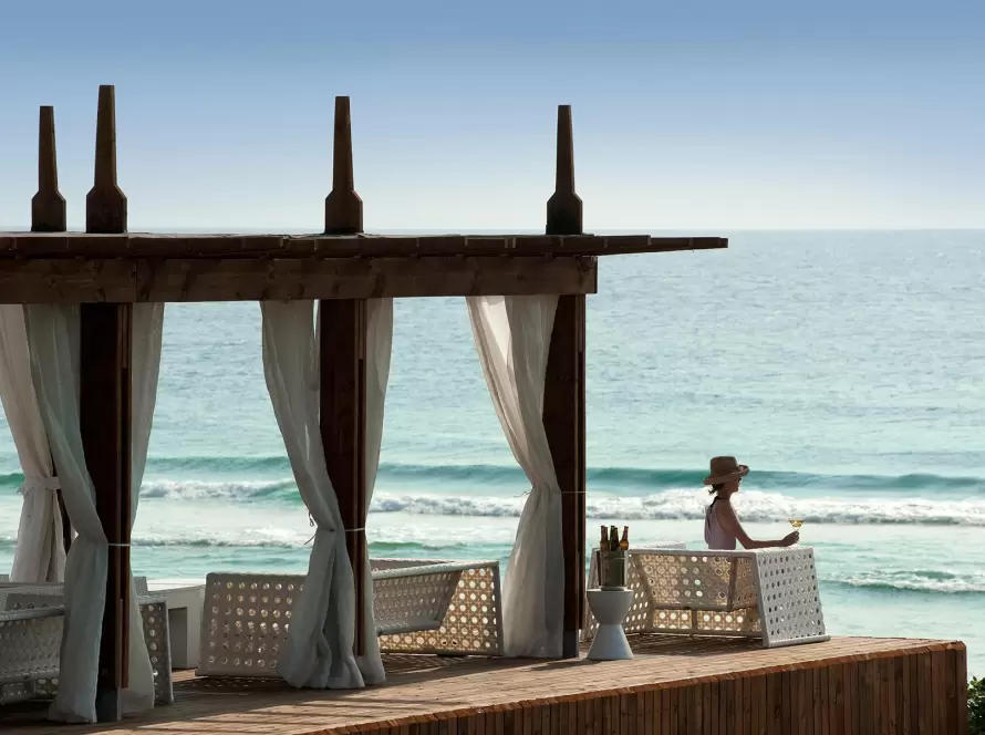 Luxury Mozambique beach resort cabana overlooking the Indian Ocean with a guest enjoying a seaside cocktail.