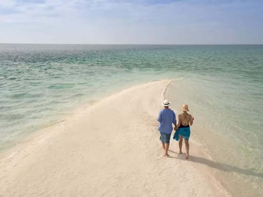 A romantic couple walking on the white sandy beaches of Mozambique’s Benguerra Island, where turquoise waters meet the sky.